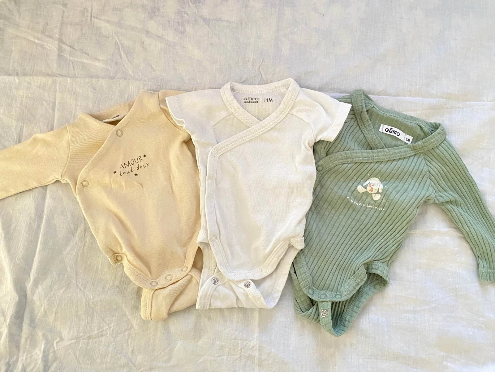 Trois bodies de bébé jaune doux, blanc et vert sauge, issus du vestiaire proposé